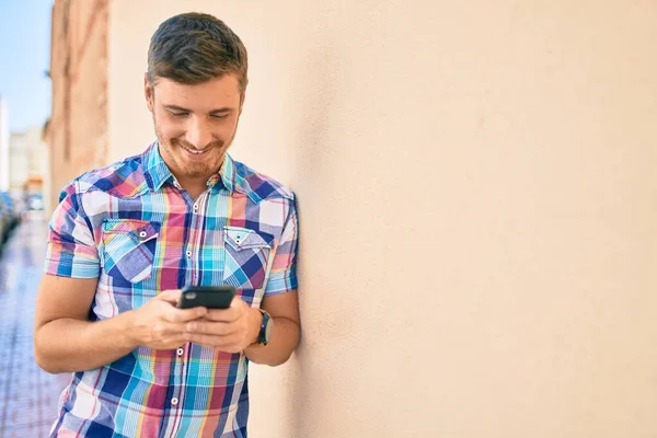 若い白人男性が市内のスマートフォンを使って笑顔で幸せ — ストック写真