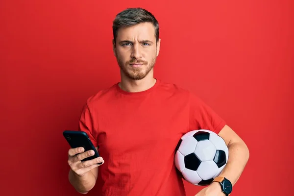 Snygg Kaukasisk Man Som Håller Fotboll Tittar Smartphone Skeptisk Och — Stockfoto