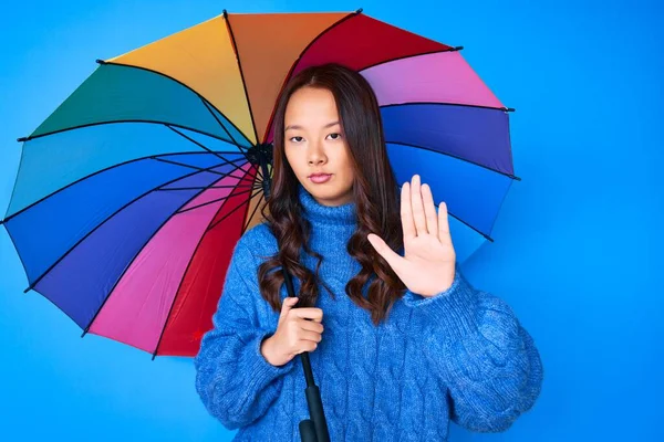 年轻美丽的中国姑娘手握五彩缤纷的雨伞 做了个手势 表情严肃而自信 做手势防守 — 图库照片