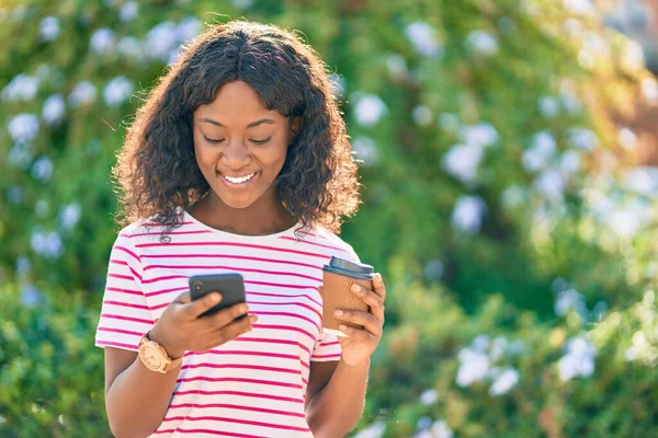 Genç Afrikalı Amerikalı kız akıllı telefon kullanıyor parkta kahve içiyor..