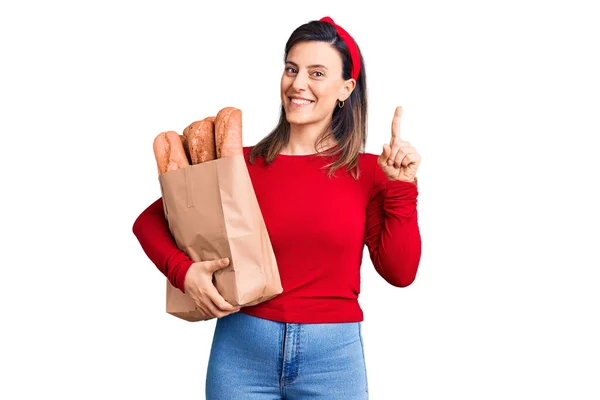 若いです美しい女性保持紙袋パンとともに驚きでアイデアや質問を指差す指で幸せな顔 ナンバーワン — ストック写真
