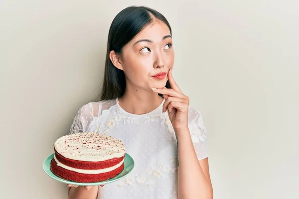 Młoda Chinka Trzymająca Tort Marchewkowy Poważna Twarz Myśląca Pytaniu Ręką — Zdjęcie stockowe