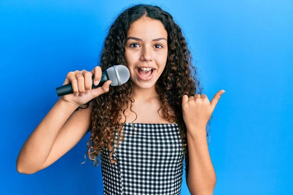 Adolescente Chica Hispana Cantando Canción Usando Micrófono Apuntando Pulgar Hacia —  Fotos de Stock