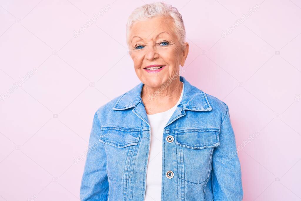 Senior beautiful woman with blue eyes and grey hair wearing casual denim jacket looking positive and happy standing and smiling with a confident smile showing teeth 
