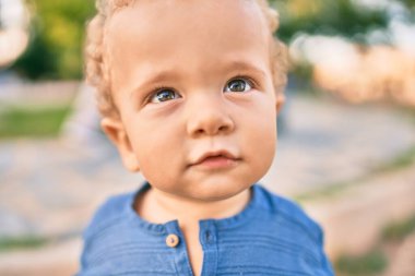 Sevimli ve mutlu küçük çocuk güneşli bir günde parkta eğleniyor. Güzel sarı saçlı erkek çocuk dışarıda oynuyor.