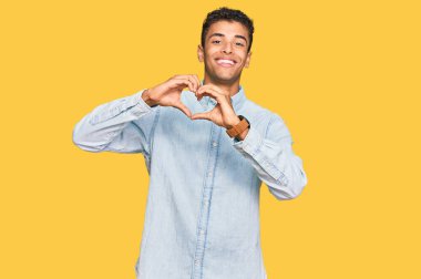 Genç, yakışıklı, Afro-Amerikalı sıradan kıyafetler giyen, aşık gülümseyen, elleriyle kalp sembolü yapan bir adam. romantik kavram. 