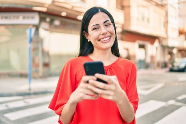 Genç Latin kız şehirde akıllı telefon kullanarak mutlu bir şekilde gülümsüyor..