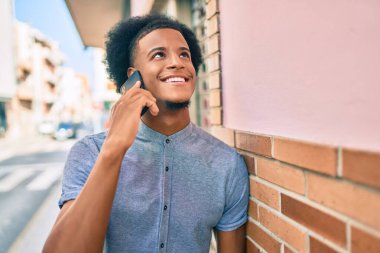 Genç Afrikalı Amerikalı gülümseyen mutlu bir adam şehirdeki akıllı telefondan konuşuyor..