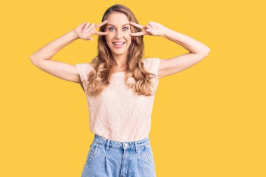 Sarışın, güzel, beyaz bir kadın. Gündelik kıyafetler giyiyor. Barış sembolü yapıyor. 