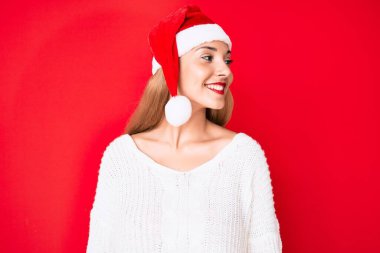 Genç esmer kadın Noel şapkası takıyor. Yüzünde gülümsemeyle yan yana bakıyor. Doğal bir ifade. Kendinden emin gülen. 