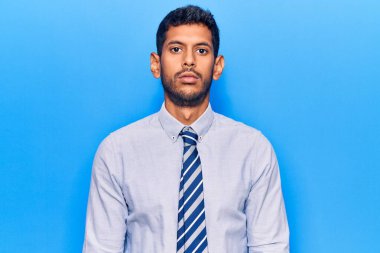 Yüzünde ciddi bir ifade olan iş kıyafetleri giyen genç bir latin. Basit ve doğal bir şekilde kameraya bakıyorsun.. 