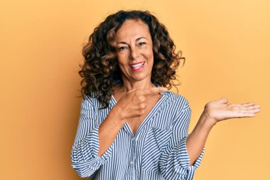 Orta yaşlı İspanyol kadın gündelik giysiler giyip kameraya hayret ediyor ve gülümsüyor.. 