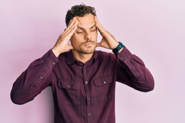 Latin asıllı genç bir adam elleri kafasında günlük kıyafetler giyiyor, stres yüzünden baş ağrısı çekiyor. migren ağrısı. 