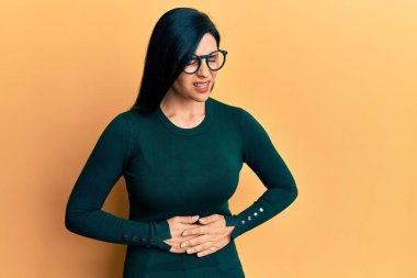 Mide bulantısı, acı verici bir hastalık yüzünden günlük giysiler ve elleri göbeğinde gözlük takan beyaz bir kadın. Ağrı kavramı. 