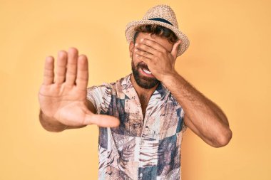 Yaz şapkası takan genç İspanyol adam elleriyle gözlerini kapatıyor ve üzgün ve korku ifadeleriyle jest yapıyor. utangaç ve olumsuz kavram. 
