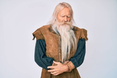 Gri saçlı ve uzun sakallı yaşlı bir adam midesi üstünde Viking kostümü giyiyor çünkü hazımsızlık, acı verici bir hastalık, kendini iyi hissetmiyor. Ağrı kavramı. 