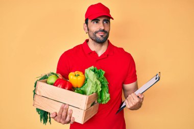 Yakışıklı, sakallı, üniformalı, elinde teslimat yemeği tutan, gülümseyen ve düşüncelere dalan bir İspanyol.. 