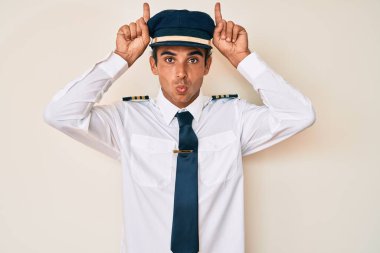 Uçak pilotu üniforması giyen genç İspanyol adam boynuz gibi parmağıyla komik hareketler yapıyor. 