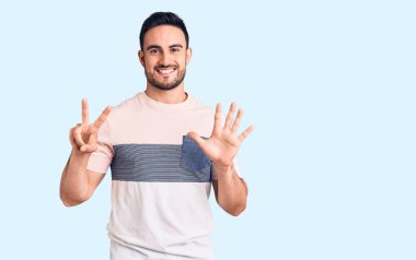 Genç ve yakışıklı bir adam gündelik giysiler giyer ve yedinci parmaklarını göstererek gülümserken kendinden emin ve mutlu olur.. 