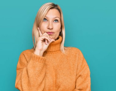 Orta yaşlı beyaz kadın, elleri çenesinde sıradan bir kazak giyiyor soru sormayı düşünüyor, düşünceli bir ifade. Gülümseyen ve düşünceli bir yüz. şüphe kavramı. 