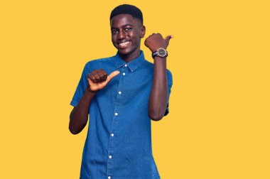 Gündelik giysiler giymiş genç Afro-Amerikan bir adam arka tarafı işaret ediyor. Elleri havada, kendinden emin gülümsüyor. 