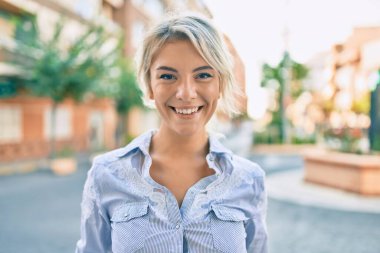 Genç sarışın kadın gülümseyerek şehirde mutlu mesut yürüyor..