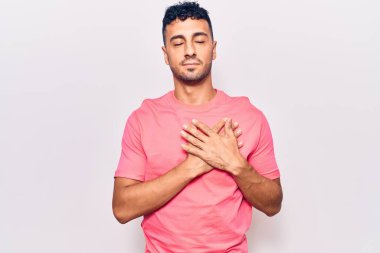 Gündelik kıyafetler giyen genç İspanyol adam elleri göğsünde gülümsüyor, gözleri kapalı ve yüzünde minnet ifadesi var. sağlık kavramı. 