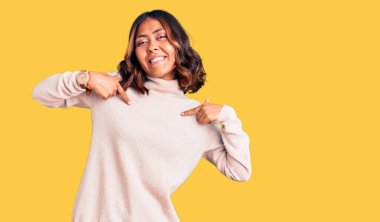 Genç, güzel, melez, balıkçı yaka kazak giyen, kendine güvenen, gülümseyen, kendini gururlu ve mutlu gösteren bir kadın.. 