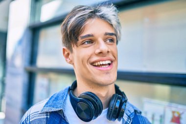 Genç İspanyol adam şehirde yürürken kulaklık takarak mutlu bir şekilde gülümsüyor..