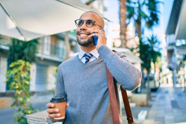 Genç Afrikalı Amerikalı iş adamı akıllı telefondan konuşuyor ve şehirde kahve içiyor..