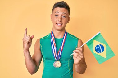 Spor kıyafetleri giyen ve Brezilya bayrağı taşıyan genç İspanyol çocuk bir fikir veya soruyla gülümsüyor ve mutlu bir yüzle işaret ediyor. 