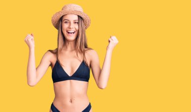 Bikini ve şapka giyen genç ve güzel bir kız kollarını kaldırıp, gözleri açık bir şekilde başarıyı kutluyor. Kazanan konsept. 