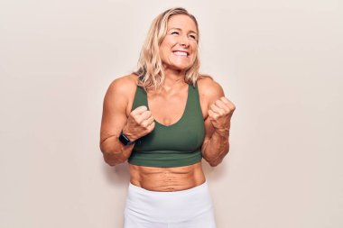 Orta yaşlı beyaz kadın spor kıyafetleri giyiyor. Kolları havada ve gözleri kapalı zaferi kutlarken gülümsüyor. Kazanan konsept. 