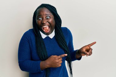 Örgülü genç siyahi kadın parmaklarını kenarı göstererek çılgınlığı kutluyor ve başarı için hayrete düşmüş gözleri açık heyecanla bağırıyor.. 