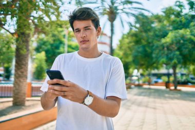 Parkta akıllı telefon kullanan rahat yüzlü beyaz bir genç..