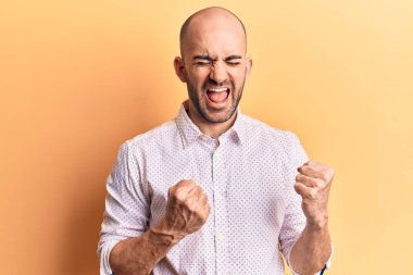 Zarif bir gömlek giyen yakışıklı kel adam şaşkınlık ve şaşkınlık içinde kollarını kaldırarak ve gözlerini kapayarak başarıyı kutluyor. 