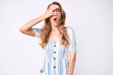 Sarışın, yaz elbisesi giymiş genç, beyaz bir kadın. Şoka girmiş, yüzünü ve gözlerini eliyle kapatmış, parmaklarından korkuyla bakıyor. 