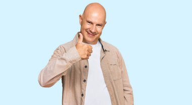 Orta yaşlı, kel, sıradan kıyafetler giyen mutlu baş parmaklar hareketi yapan bir adam. Kameraya bakıp başarıyı gösteren ifade. 