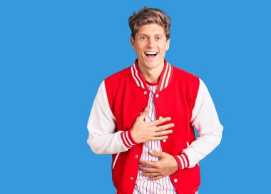 Beyzbol forması giyen yakışıklı bir genç adam gülümseyerek ve kahkahalarla gülüyor çünkü elleri vücutta komik bir şaka yapıyor.. 