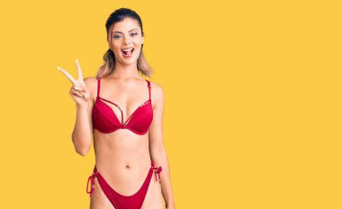 Bikini giyen, gülümseyen, kameraya göz kırpan, parmaklarıyla zafer işareti yapan güzel bir kadın. İki numara.. 