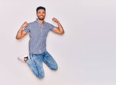 Genç, yakışıklı, sıradan kıyafetler giyen, mutlu gülümseyen bir İspanyol. Yüzünde tebessümle zıplıyor, beyaz arka planda yumruklar havada kutluyor.