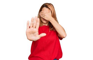 Latin kökenli genç bir kadın, gündelik kırmızı tişört giyip elleriyle gözlerini kapatıyor ve üzgün ve korku ifadeleriyle jest yapıyor. utangaç ve olumsuz kavram. 
