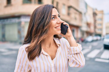 Genç İspanyol kadın gülümsüyor. Şehirdeki akıllı telefondan konuşuyor..