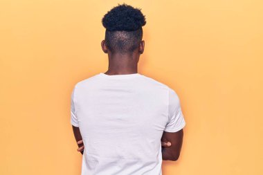 Gündelik giysiler giymiş genç Afro-Amerikan bir adam arkasını dönüp kollarını kavuşturarak başka tarafa bakıyor. 