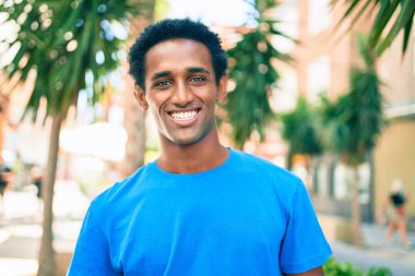 Yakışıklı siyah Afrikalı adam dışarıda mutlu gülümsüyor.