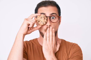 Genç yakışıklı adam elinde kurabiyeyle ağzını kapatıyor. Şok olmuş ve hata yapmaktan korkuyor. şaşırmış ifade 