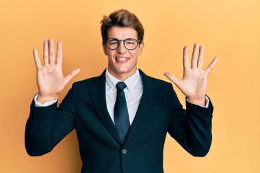 İş elbisesi ve kravat takan yakışıklı beyaz adam on numarayı gösterip işaret ederken kendinden emin ve mutlu gülümsüyor.. 