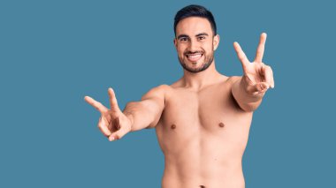 Mayo giymiş, ağzı açık gülümseyen genç ve yakışıklı bir adam zafer işareti yaparken iki elini de gösteriyor. İki numara.. 