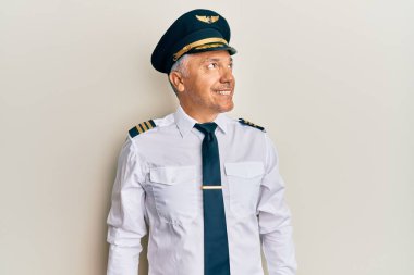 Yakışıklı, orta yaşlı, uçak pilotu üniforması giyen, yüzünde gülümsemeyle yan yana bakan, doğal bir ifade. Kendinden emin gülen. 