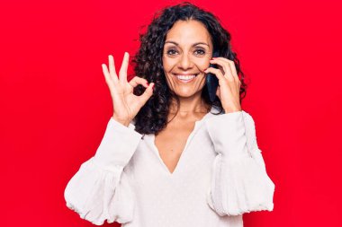 Orta yaşlı güzel bir kadın akıllı telefondan konuşuyor parmaklarıyla işaret veriyor, gülümsüyor ve mükemmel bir sembol oluşturuyor. 
